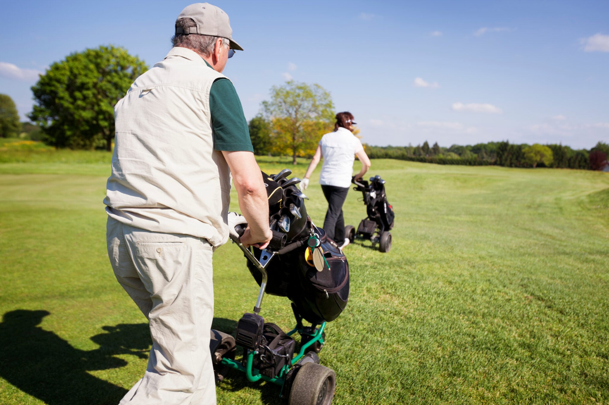 Golfers pushing trolleys on a golf course | Source: Adobe Stock