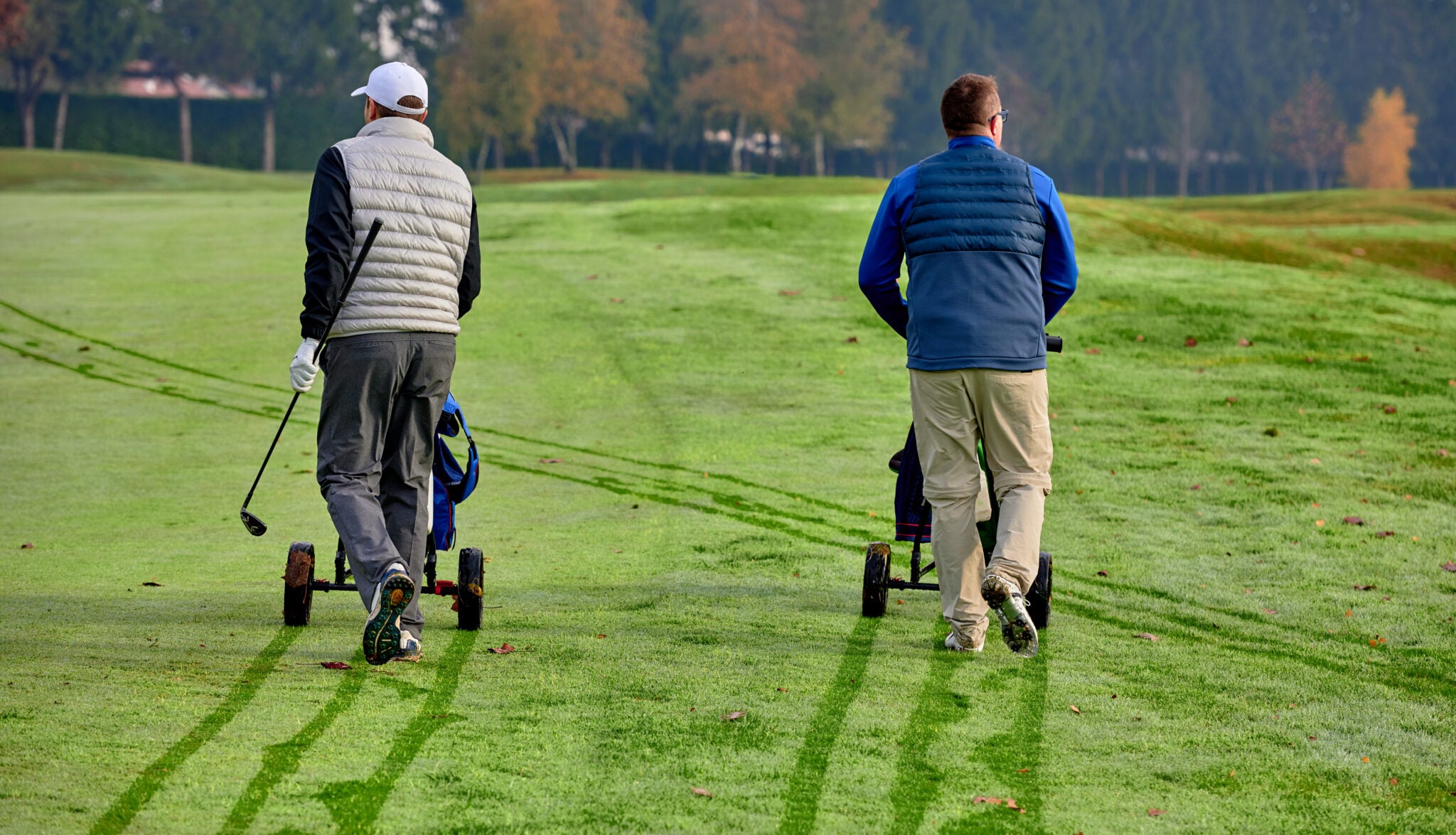 Golfers wheel their trolleys through the dew during winter golf | Source: Adobe Stock